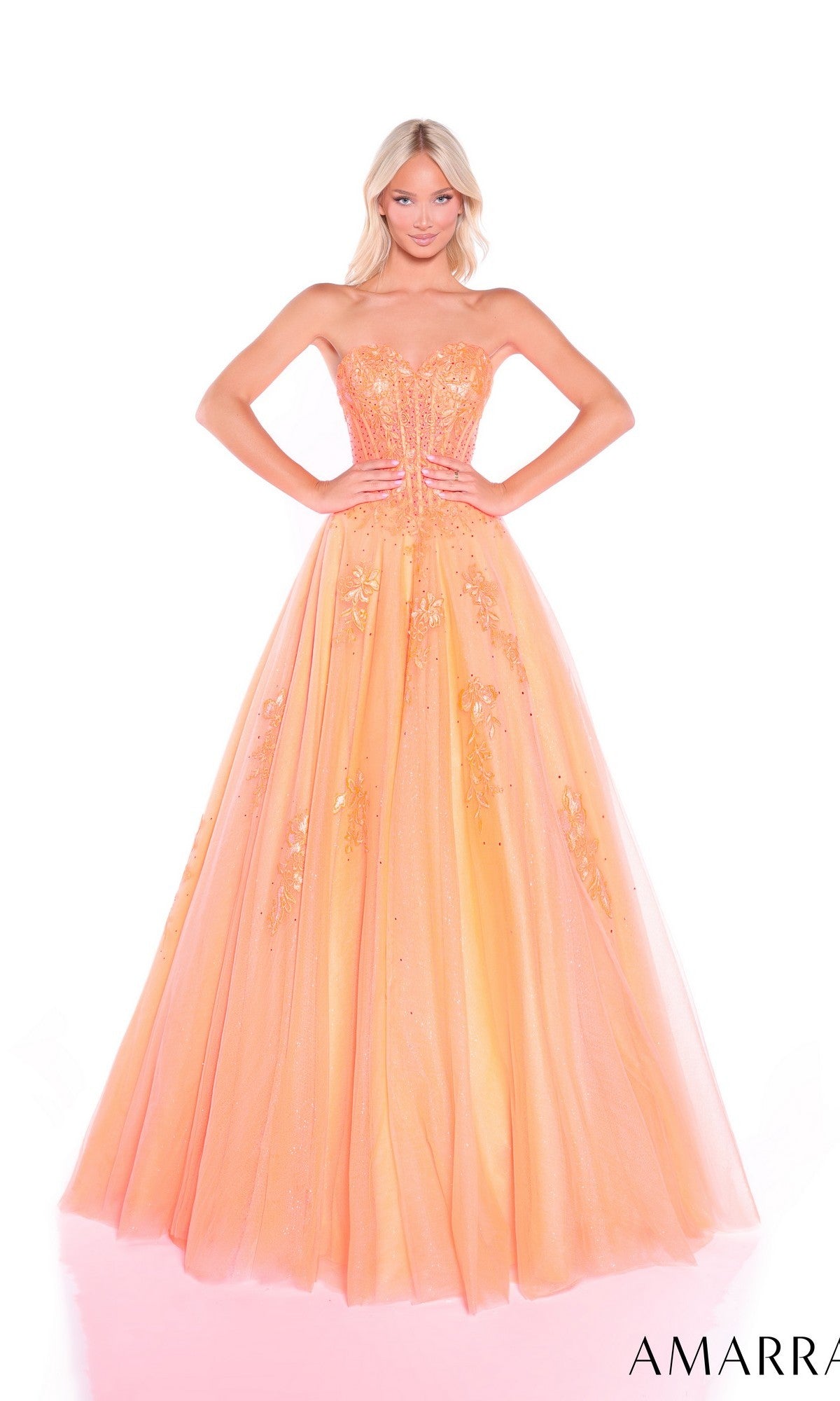 A woman stands confidently with hands on hips in a peach Lace-Up Strapless Prom Ball Gown, Amarra 89011, featuring a sweetheart bodice and floral embellishments against a white background.